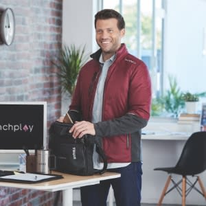 A man standing infront of the desk holding a labtop  bag