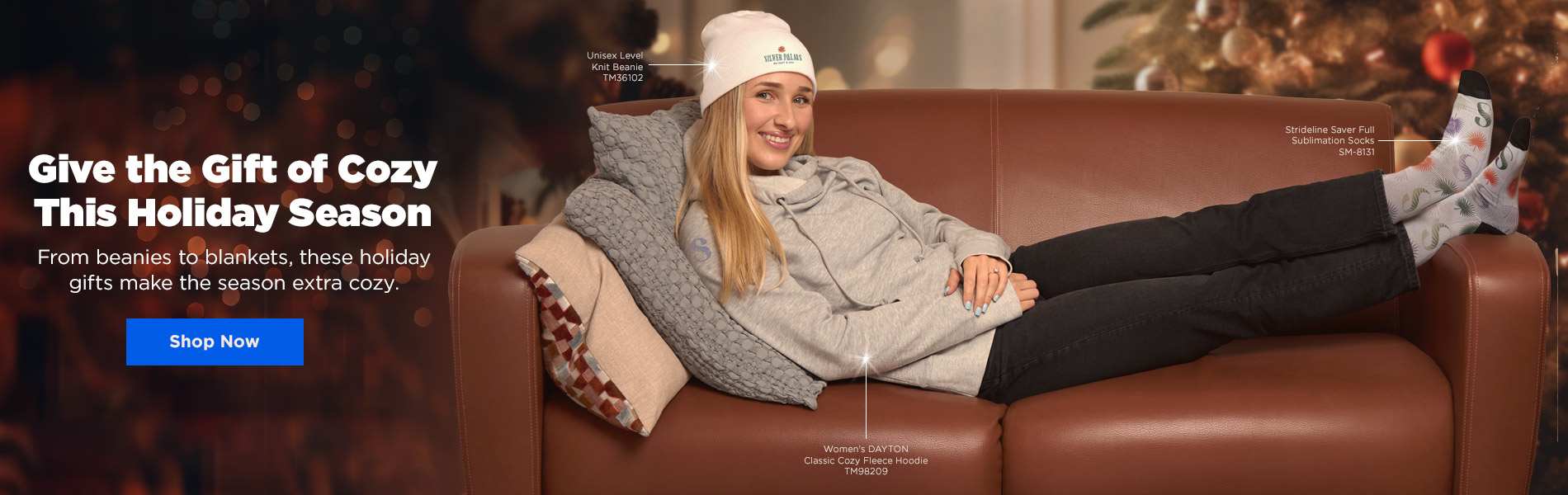 Woman lounging on sofa wearing cozy beanie, fleece hoodie, and sublimation socks with holiday gifting message and Shop Now button.